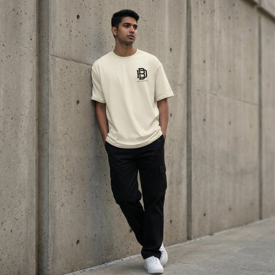 Man wearing an offwhite Oversized t-shirt with a logo and black pants leaning against a concrete wall.
