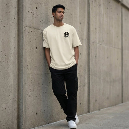 Man wearing an offwhite Oversized t-shirt with a logo and black pants leaning against a concrete wall.