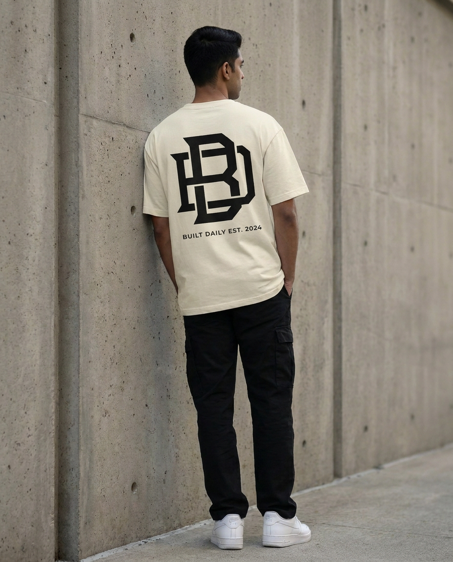 Person wearing a off white Oversized t-shirt with a logo and text, standing against a concrete wall.